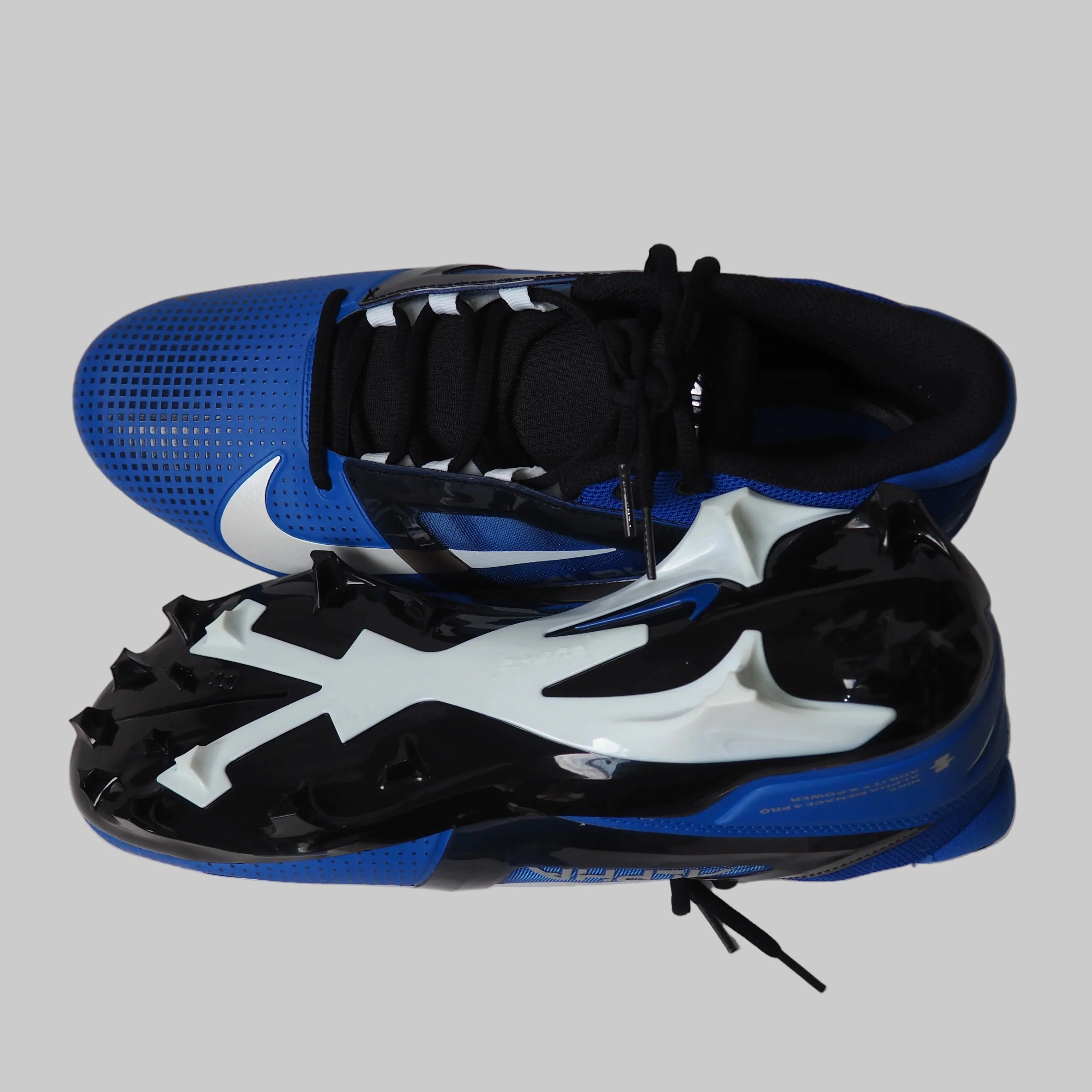 Top and sole view of blue and black Nike Alpha Menace Pro 4 football cleats with white swoosh and black cleat plate on a light gray background.